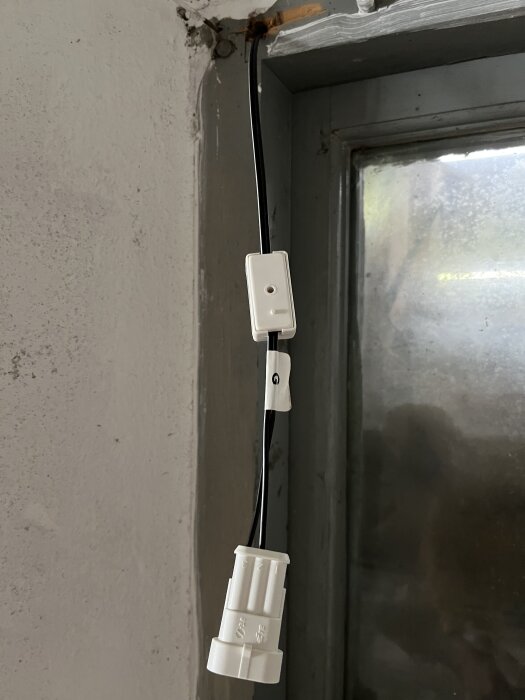 En vit elkoppling och en kabel hänger vid ett fönster i ett renoveringsprojekt.