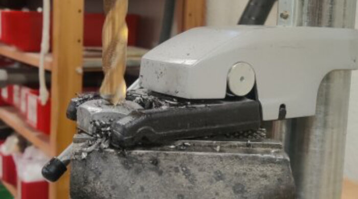 Bild på en mystisk hållare monterad på en pelarborr, omgiven av metallspån i en verkstadsmiljö.