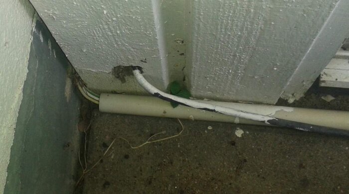 Elektrisk installation med kablar går genom vägg i hörn, tecken på slitage och felmontering.