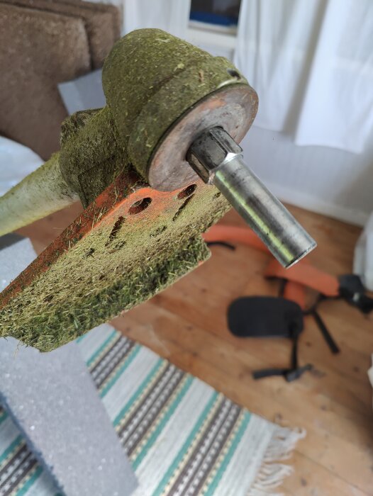 Närbild av axeln på en trimmer med växelhuset delvis täckt av klipprester. Axeln ser ut att behöva modifieras för att fästa en klinga.