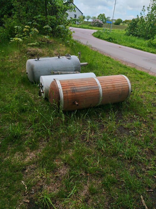 Gamla borttagna värmepannor ligger på en gräsplätt vid en kurvande väg.