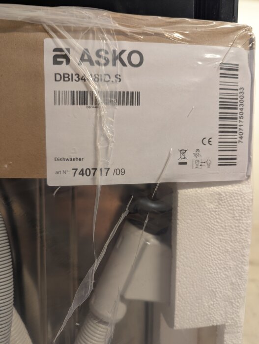 Förpackning av en Asko diskmaskin, modell DBI34BI8ID.S, visas med synlig etikett och streckkod i plastad kartong.