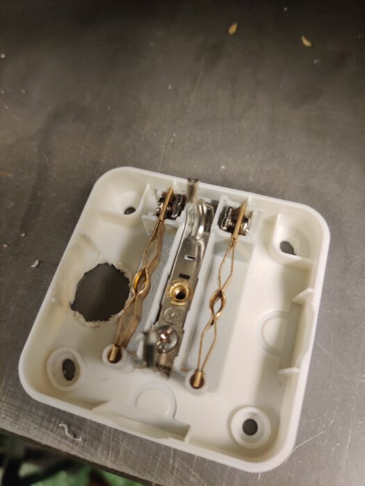Öppet eluttag med skruvanslutningar och metallbleck instuckna mellan plastflärpar, visande bristande konstruktion på ett bord.
