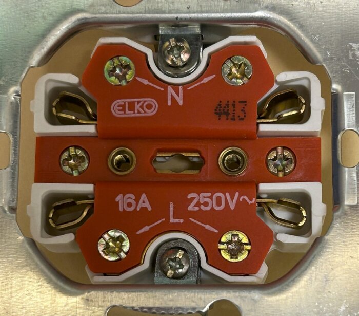 Bild på ett ELKO vägguttag med märkningen 16A 250V, markerad med N och L för ledningarna, monterad på en metallplatta.