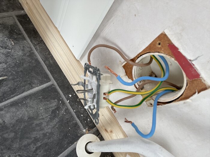 Elektrisk kopplingsdosa med sladdar, inkl. brun och blå sladd, där en vit spak syns och en sladd är fortfarande fast.