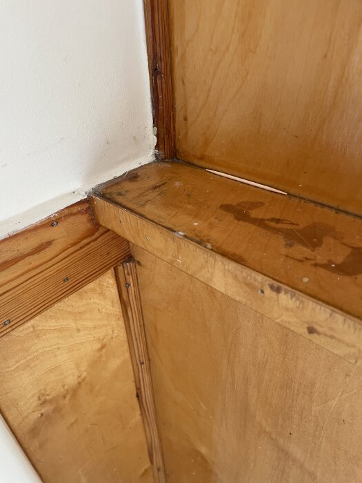 Köksskåp fastspikat mot en vit vägg, visar hörndetalj och trästrukturer från insidan i ett gammalt hus.