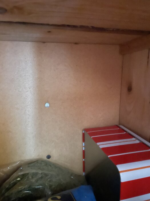 Invändig vy av ett köksskåp med en skruv synlig i träväggen samt en röd- och vitrandig metallburk på hyllplanet.