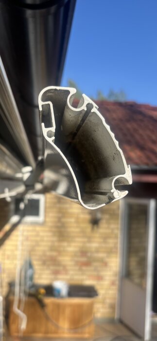 Ändprofil av en gammal Somfy markis monterad utomhus mot en klar himmel och tegelvägg i bakgrunden.