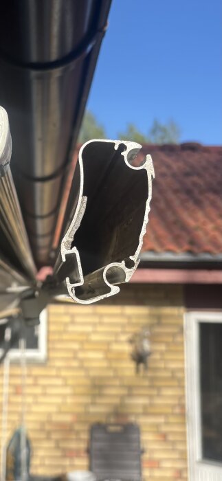 Ändprofil av Somfy markis, monterad vinkel i fokus, bakgrund med tegelvägg och tak synlig.