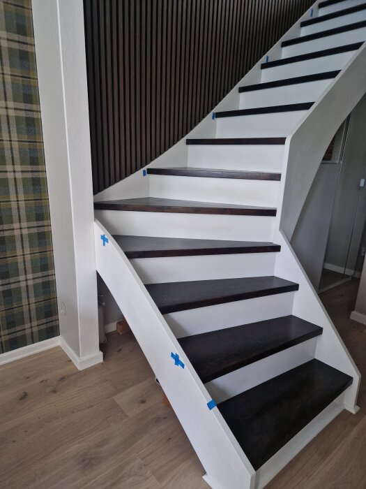 Svartvit trappa med mörka steg och vita sidostycken. Blå markeringar indikerar var stolpar ska monteras för ledstången.