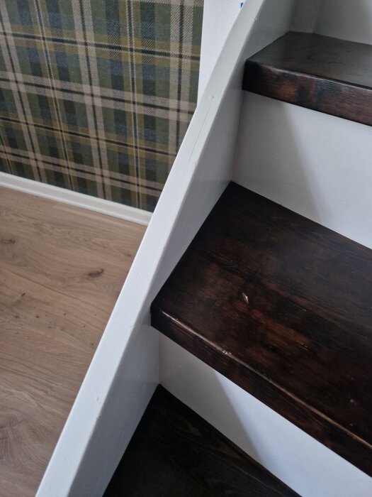 Närbild av en trappa med mörka trappsteg och vit vangstycke, med blå markeringar för montering av stolpar för en ny ledstång.