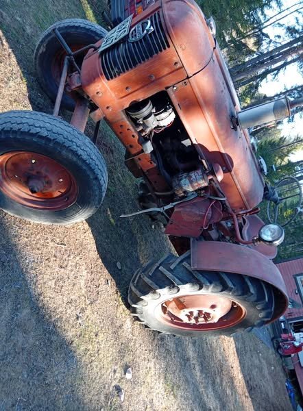 Gammal orange traktor på gräsmatta vid skog, närbild motorn, problem med startmotor 9 kuggars 6 eller 12v nämns i texten.