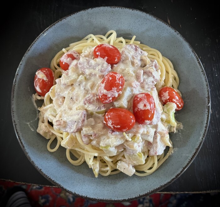 Spagetti med pastasås av bacon, salami, broccolistamm, lök, grädde och körsbärstomater på en tallrik.