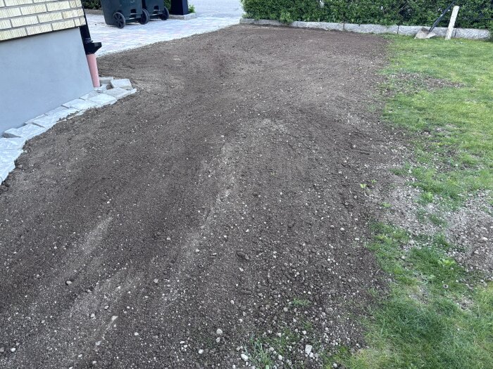 Nyutlagd jord på en gräsmatta intill ett hus med stensatt gång, omgiven av grönt gräs.