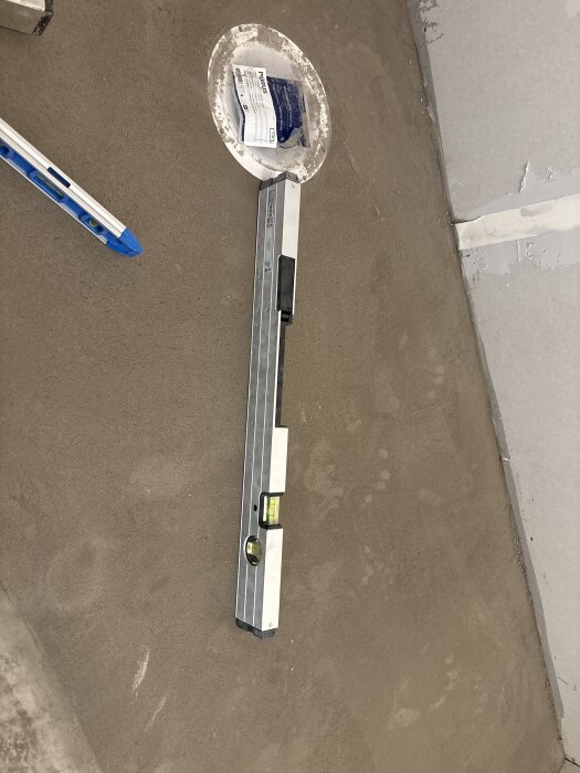 Flytspacklat golv med vattenpass och nivåpinnar, avloppsbrunnen synlig. Fokuserar på att skapa fall och jämna ytor vid renovering.