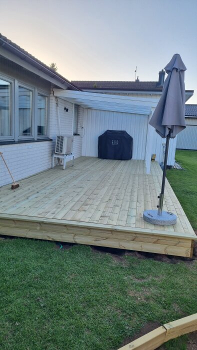 Nytt tralldäck färdigställt, med utemöbler och grill på plats, bredvid en vit målad husvägg.