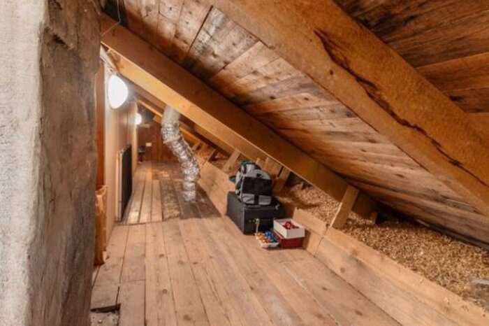 Vind med lågt snedtak och träbjälkar, packningar och ventilationsrör, del av renoveringsdiskussion om att höja taket för att få högre takhöjd.