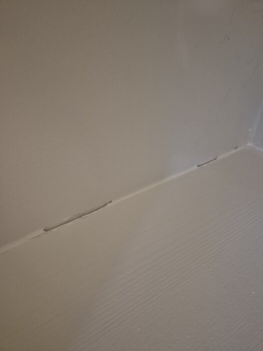 Akrylfog och målarfärg har lossnat längs en skarv efter borttagning av tejp, vilket skapar en synlig spricka på en målad yta.