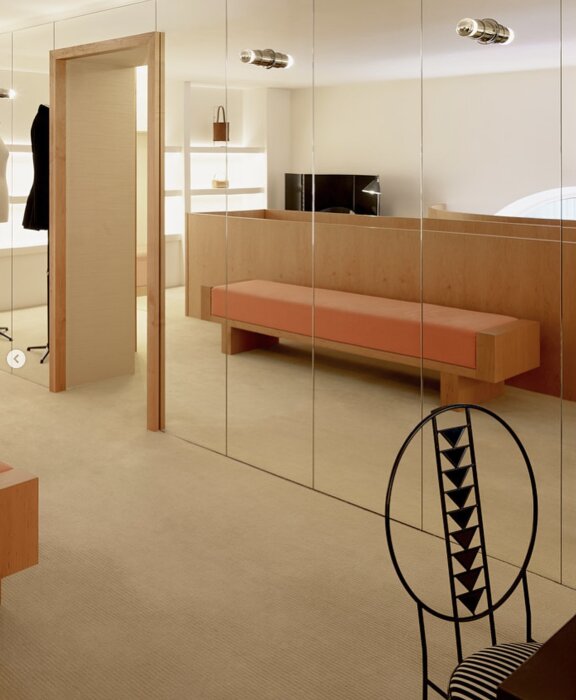 Vägg täckt med stora speglar i ett modernt rum med träinredning, orange bänk och dekorativ stol.