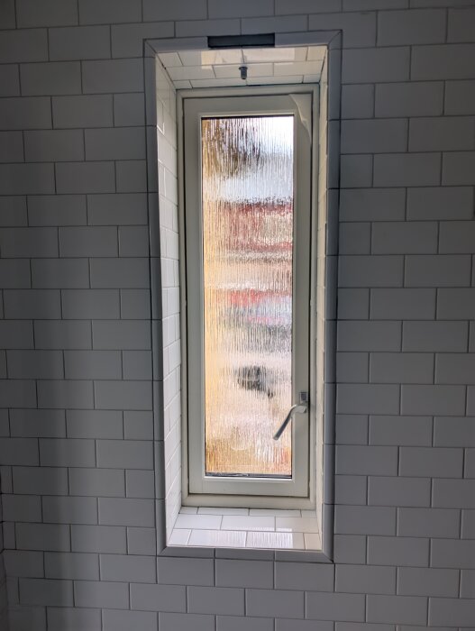 Fönster inramat av vita kakelplattor med kantlist monterad på kakelväggen.