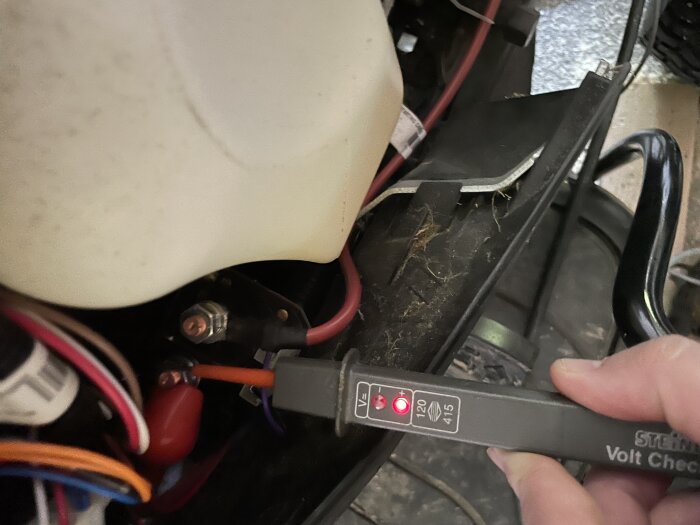 En person använder en voltmätare för att kontrollera spänningen på startsolenoiden i en åkgräsklippare.