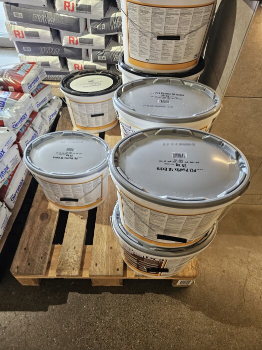 Hinkar med PCI Pavifix-bruk och påsar med Dyna-murbruk staplade på en träpall i en butik.