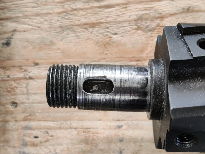 Närbild på en metallaxel med en nyligen markerad spår för kilen, monterad till en planhyvel, med en skruvtving i bakgrunden.