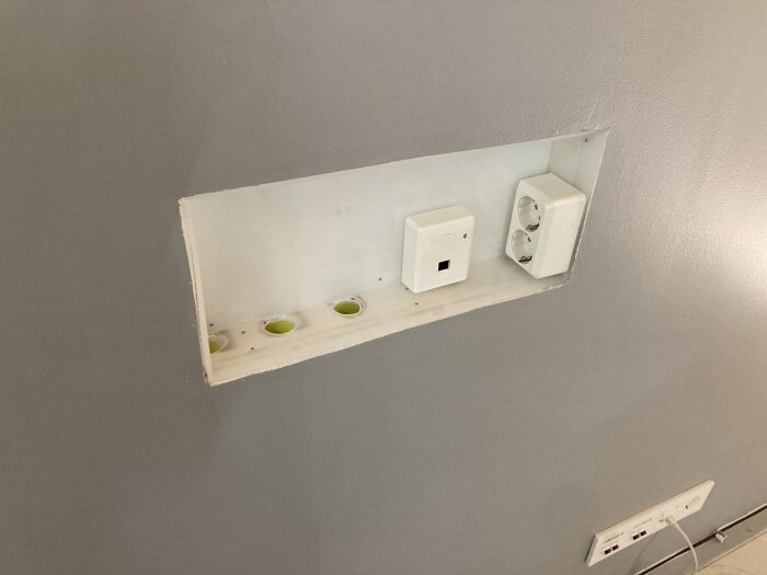 Inbyggd nisch i väggen med eluttag och strömbrytare på grå vägg.