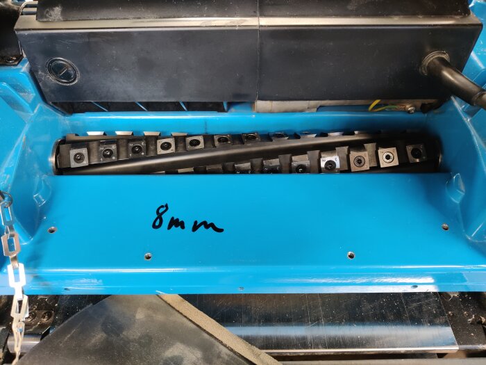 Blå planhyvel med installerad helix-cutter och märkning "8 mm", omgiven av svarta delar och knivar för träbearbetning.