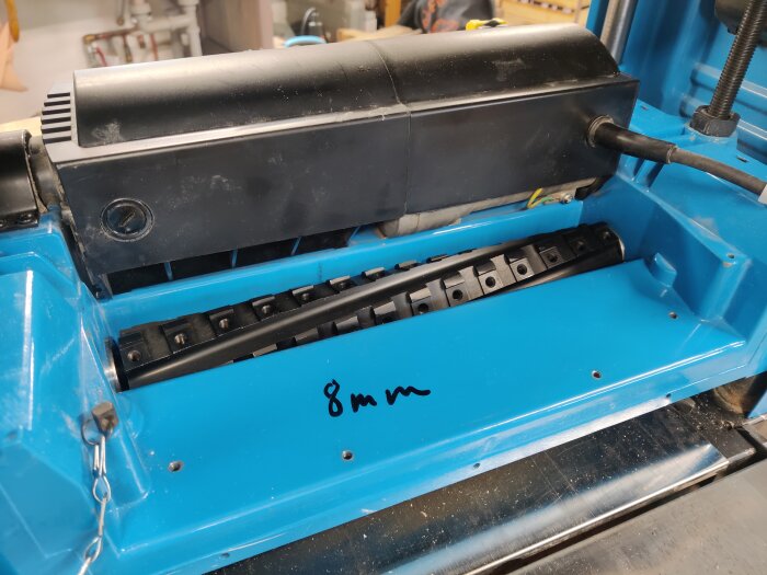 En planhyvel med installerad helix-cutter, synlig inuti en blå maskin. Det står “8 mm” på maskinens yta.