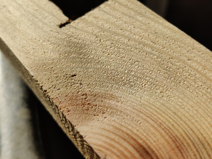 Närbild av en träyta som visar bearbetat trä med tydliga kornstrukturer och en skåra på kanten, efter användning av en helix-cutter.