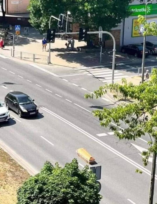 En kista placerad på en trafikerad väg, omgiven av bilar och trafikljus, med ett övergångsställe och affär i bakgrunden.