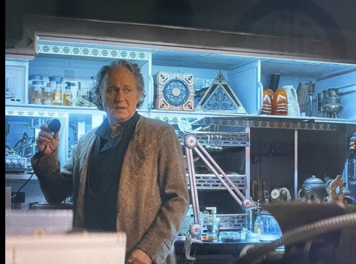 En man står framför en hylla fylld med antika föremål, inklusive Sancara-stenar, i en butiksliknande miljö.