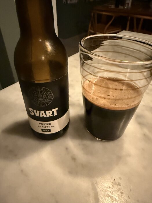 Flaska och glas med svart porteröl på ett marmorbord.