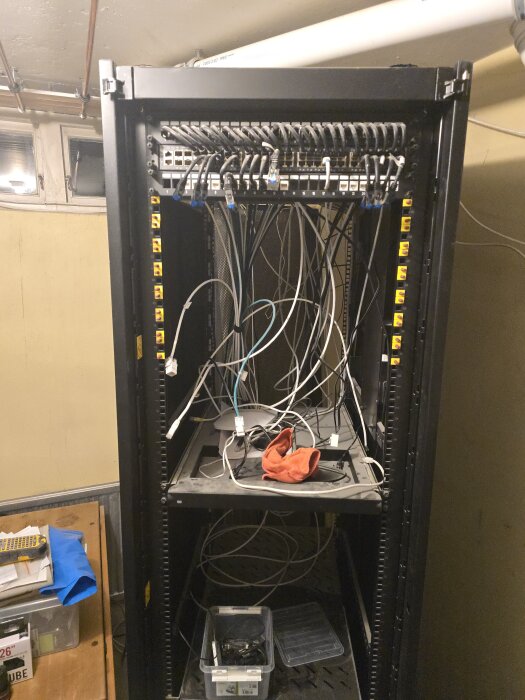 Ett 42U-serverrack med kabelhärva och dammig utrustning inklusive en 48-portsswitch, stående i ett hobbyrum under flytt till maskinrum.