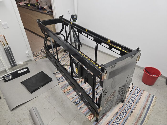 Ett demonterat serverrack ligger på trasmattor i ett hobbyrum med olika delar runtomkring, redo för att flyttas.