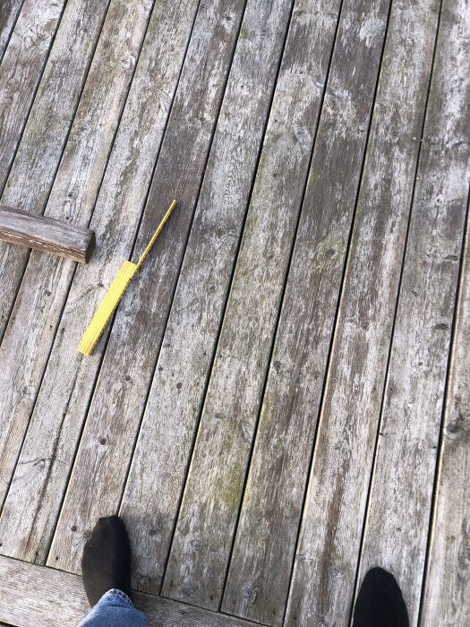 Sliten träaltan med missfärgningar och plats där ytskyddet har lossnat, delvis rengjord med sopborste, och en fot i jeans och mörk socka syns i hörnet.