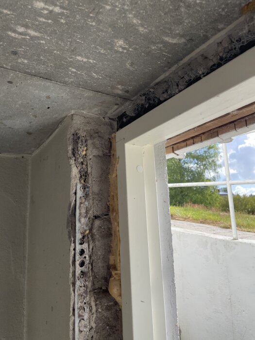 Close-up of a basement entrance showing damaged stonework and a white door frame. Sunlight and greenery visible outside through a window.