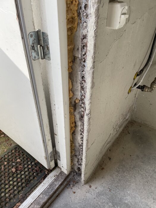 Close-up of a basement entrance showing an unfinished door frame with exposed stone and insulation, highlighting renovation needs around the door area.