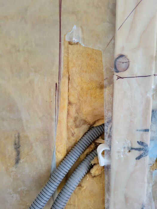 Trasig plastskydd med isolering och elledningar i ett kök under renovering, visar hål av olika storlekar.