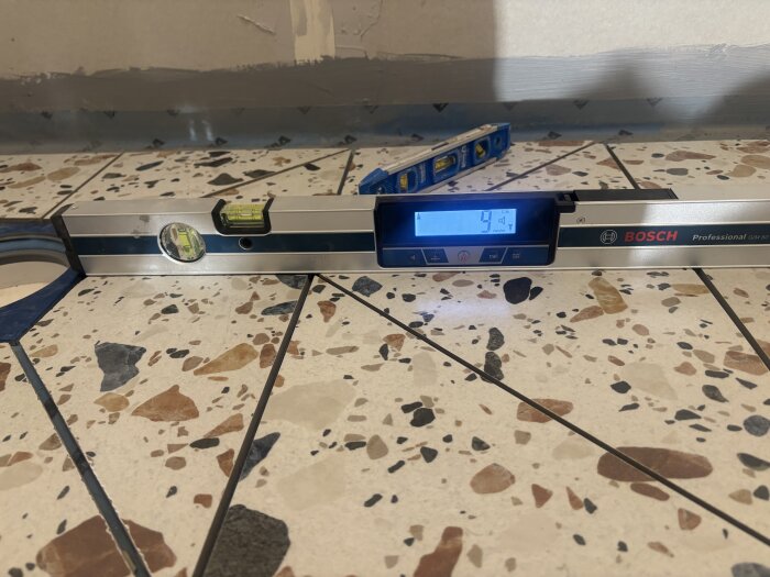 Vattenpass på stengolv visar golvets lutning, med digital display som visar 4° och ett traditionellt vattenpass i bakgrunden.