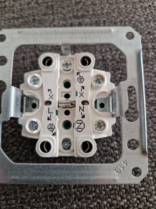 Elektriskt vägguttag med märkningar L och N för anslutning av faser och nolla, samt jordningssymbol, mot en mörk bakgrund.