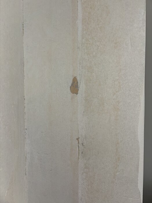 Gammal tapet med rödaktiga missfärgningar och sprickor, potentiellt orsakade av kemisk reaktion under ytan i ett radhus från 70-talet.