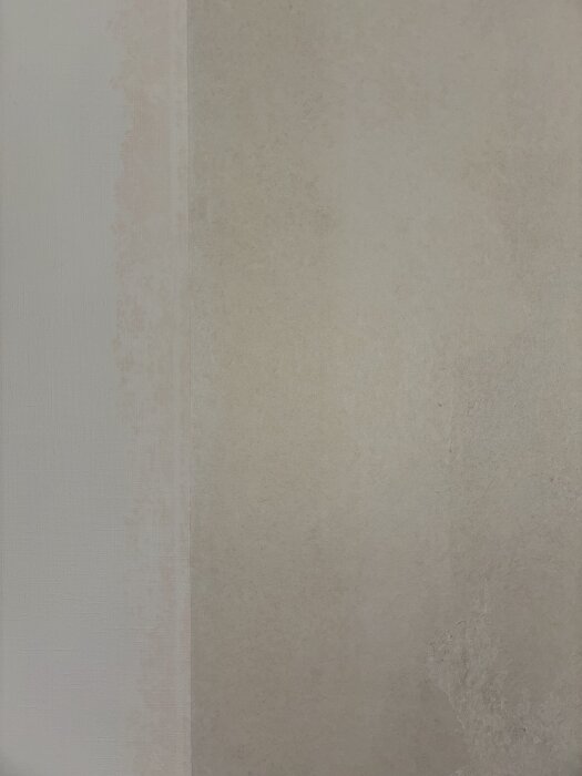 Närbild av gammal tapet på en vägg med röda flammiga missfärgningar under, utan föregående lager färg eller tapet.