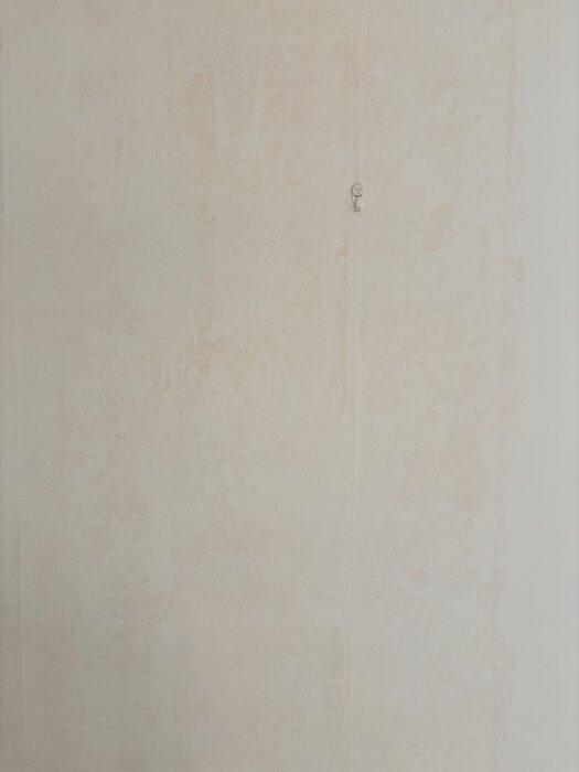 Tapet på en vägg med rödflammiga missfärgningar och en vit krok; allmän känsla av potentiell fukt- eller kemisk reaktion.