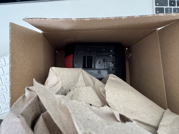 En batteri i en omärkt kartong med en annan rödfärg och dålig passform, omgiven av brunt packpapper.