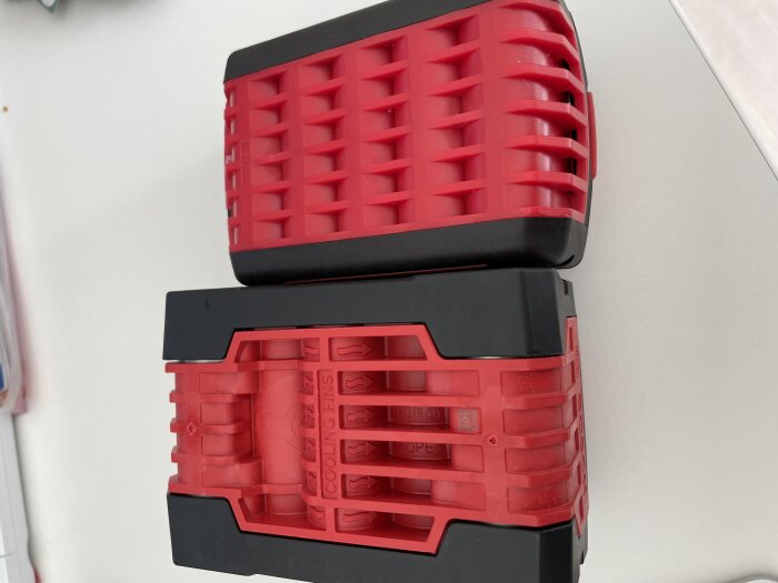 Två röda och svarta batterier staplade på varandra; den övre verkar vara ett eftermarknadsbatteri och den undre ett originalbatteri med tydligare märkning.