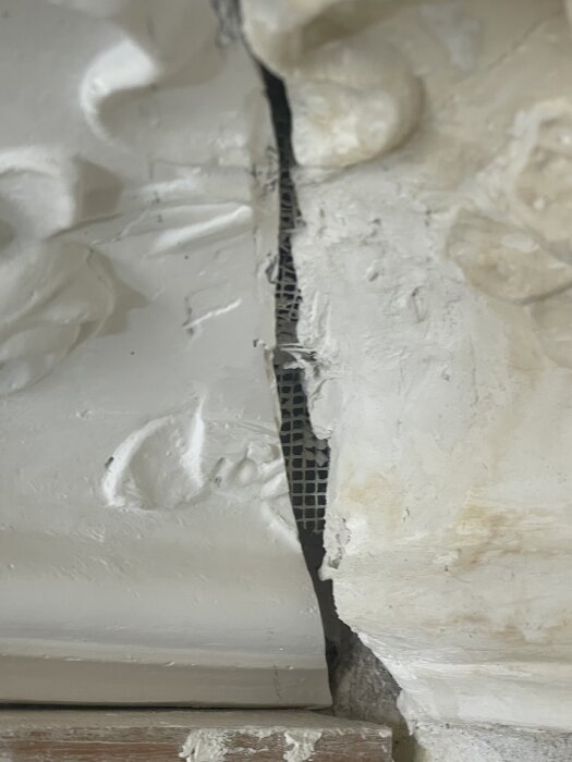 Gipsornament med synligt spackelarbete och en glipa som avslöjar nät under ytan, del av pågående renoveringsprojekt.