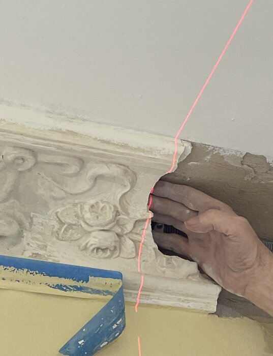 Hand justerar lister med blommönster vid tak, belyst av röd laserlinje.