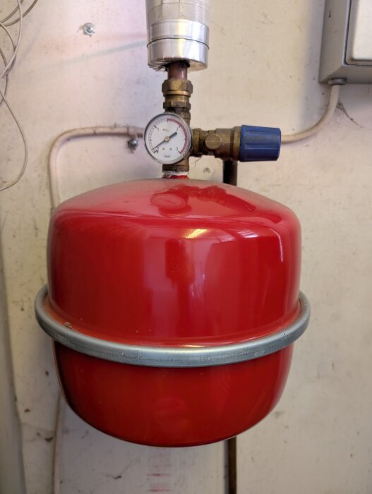 Rött expansionskärl med en tryckmätare och två ventiler, en läcker vatten och den andra släpper ut luft.